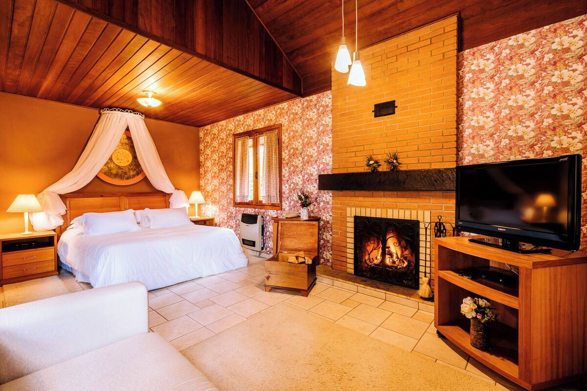 Un dormitorio con cama, mesitas de noche, televisión y chimenea.