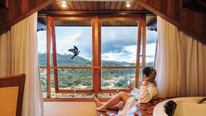 Una mujer descansando junto a una ventana con vista a un paisaje montañoso.