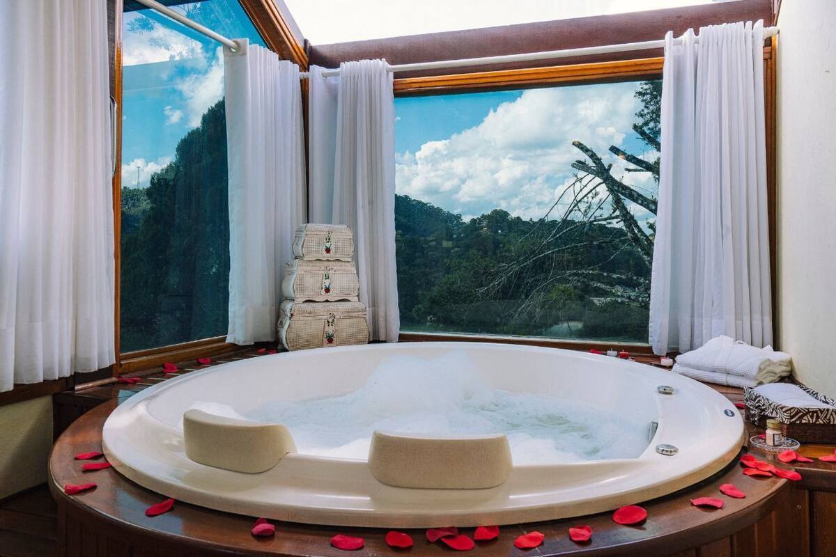 Un jacuzzi con pétalos de rosa, una banca de madera y vistas a un bosque a través de un amplio ventanal.