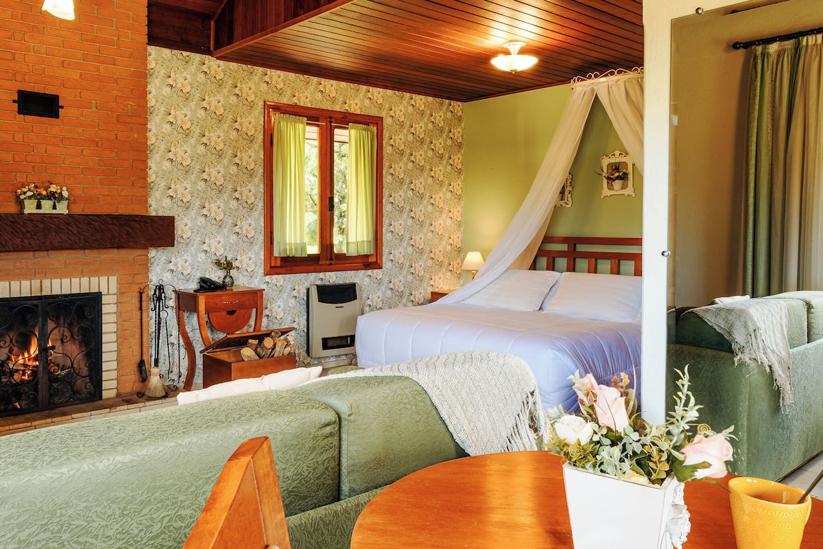 Una habitación acogedora con chimenea, una cama con dosel, un sofá verde y una mesa de madera.