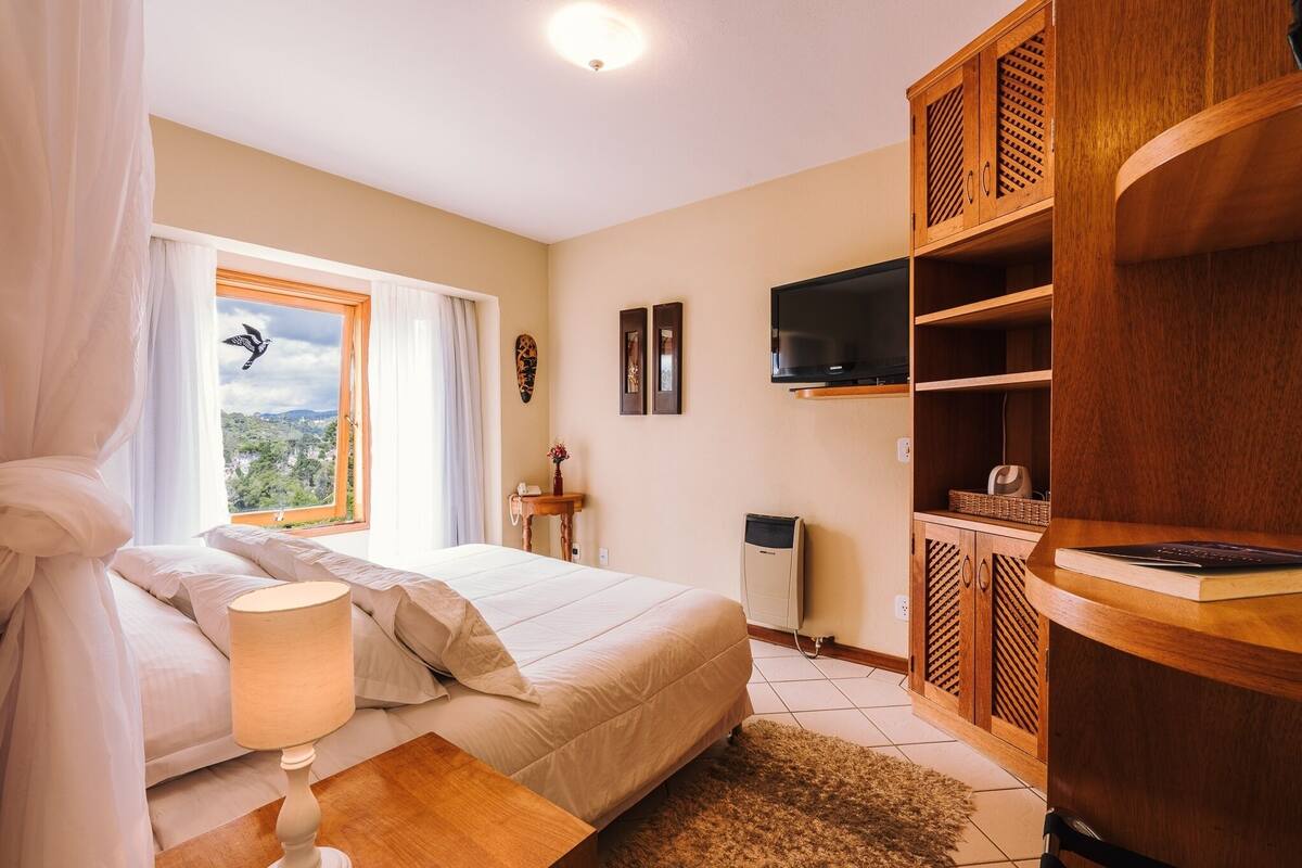 Un dormitorio con cama, lámpara de noche, armario de madera, televisor y ventana con cortinas.