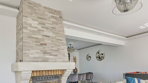 Una sala de estar moderna con chimenea de piedra, una mesa de centro de vidrio y una araña.