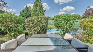 Un patio con una mesa y sillas, con vistas a una piscina y un paisaje verde.