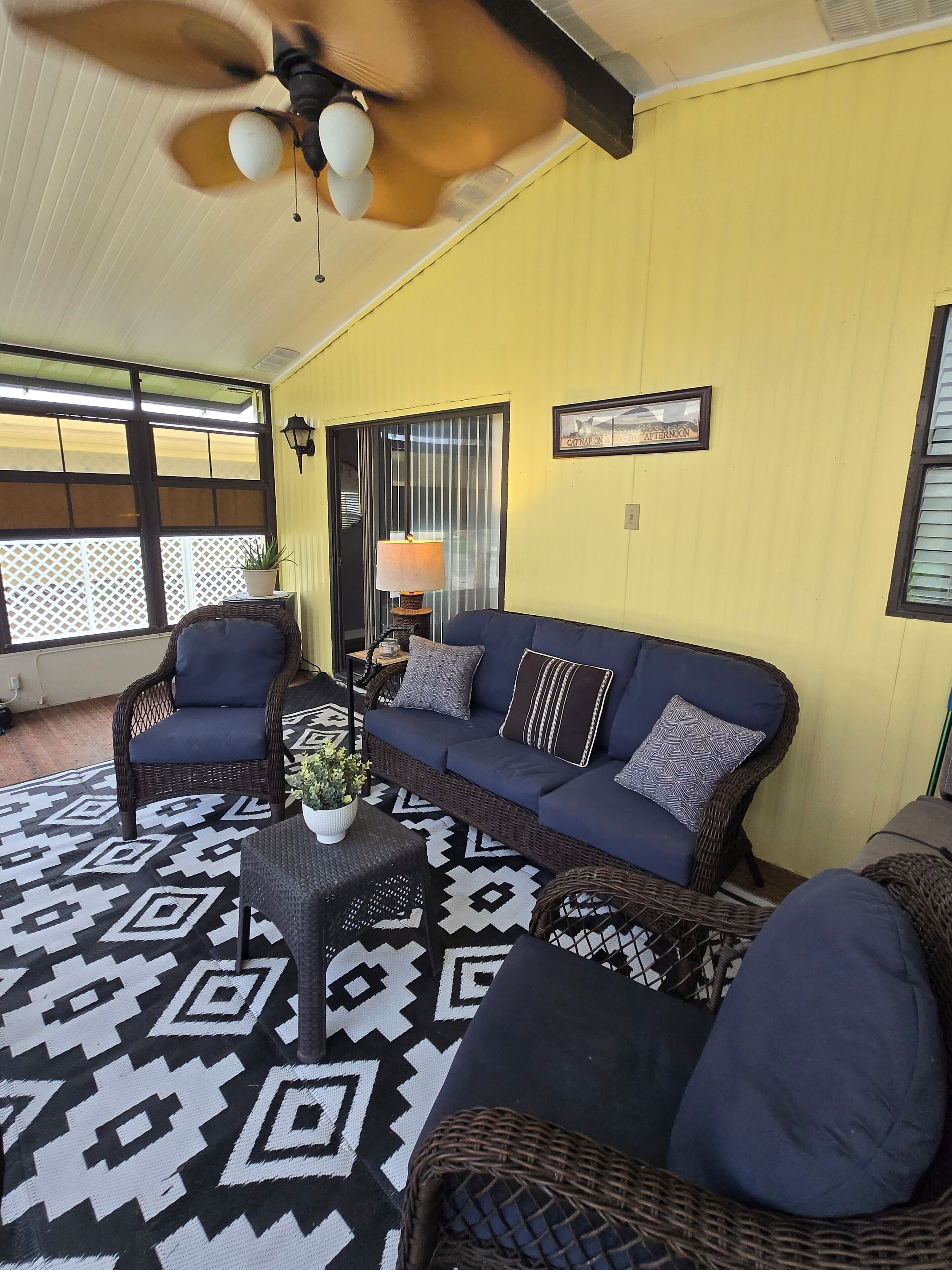 A cozy room with a blue sofa, wicker chairs, a patterned rug, and a ceiling fan.