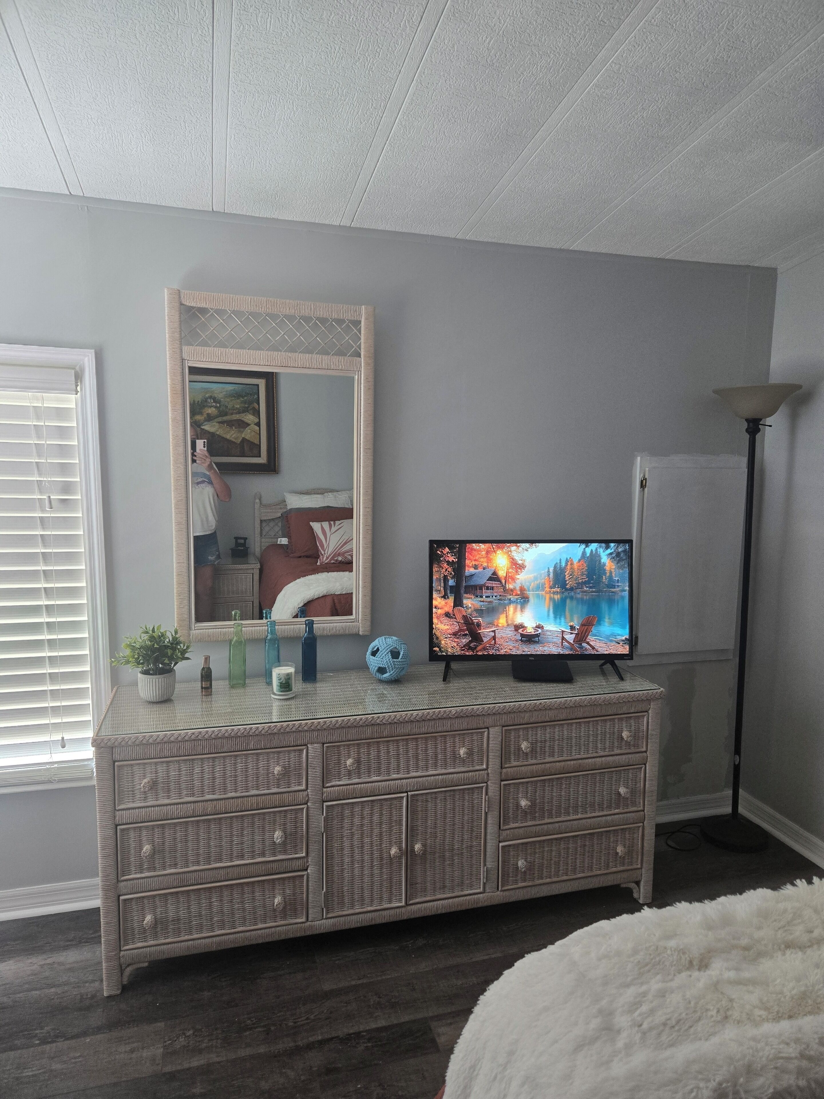 Une pièce comprenant une console en osier, un téléviseur à écran plat, un grand miroir et un lampadaire.