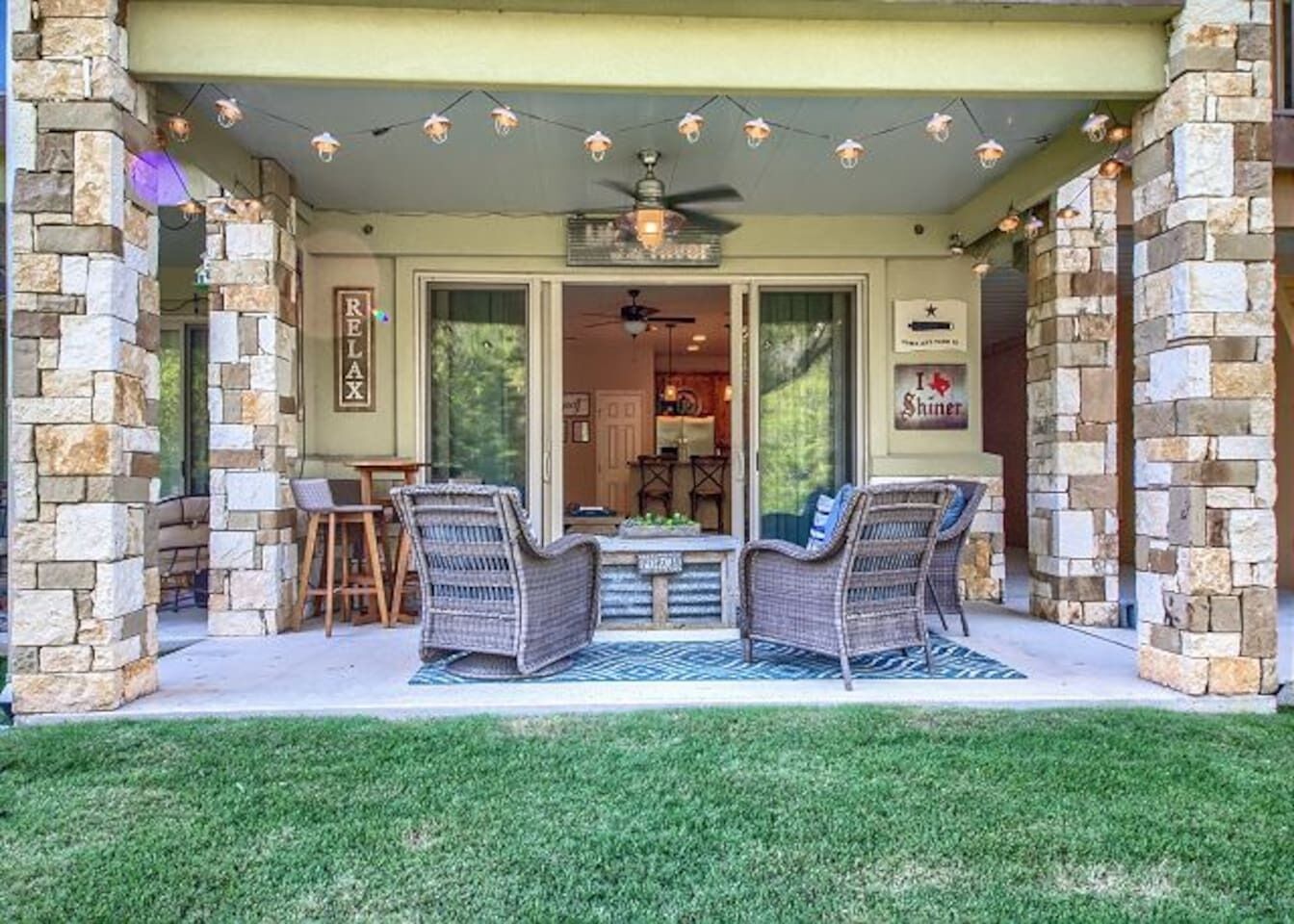 A covered patio with wicker furniture, stone walls, and a ceiling fan.