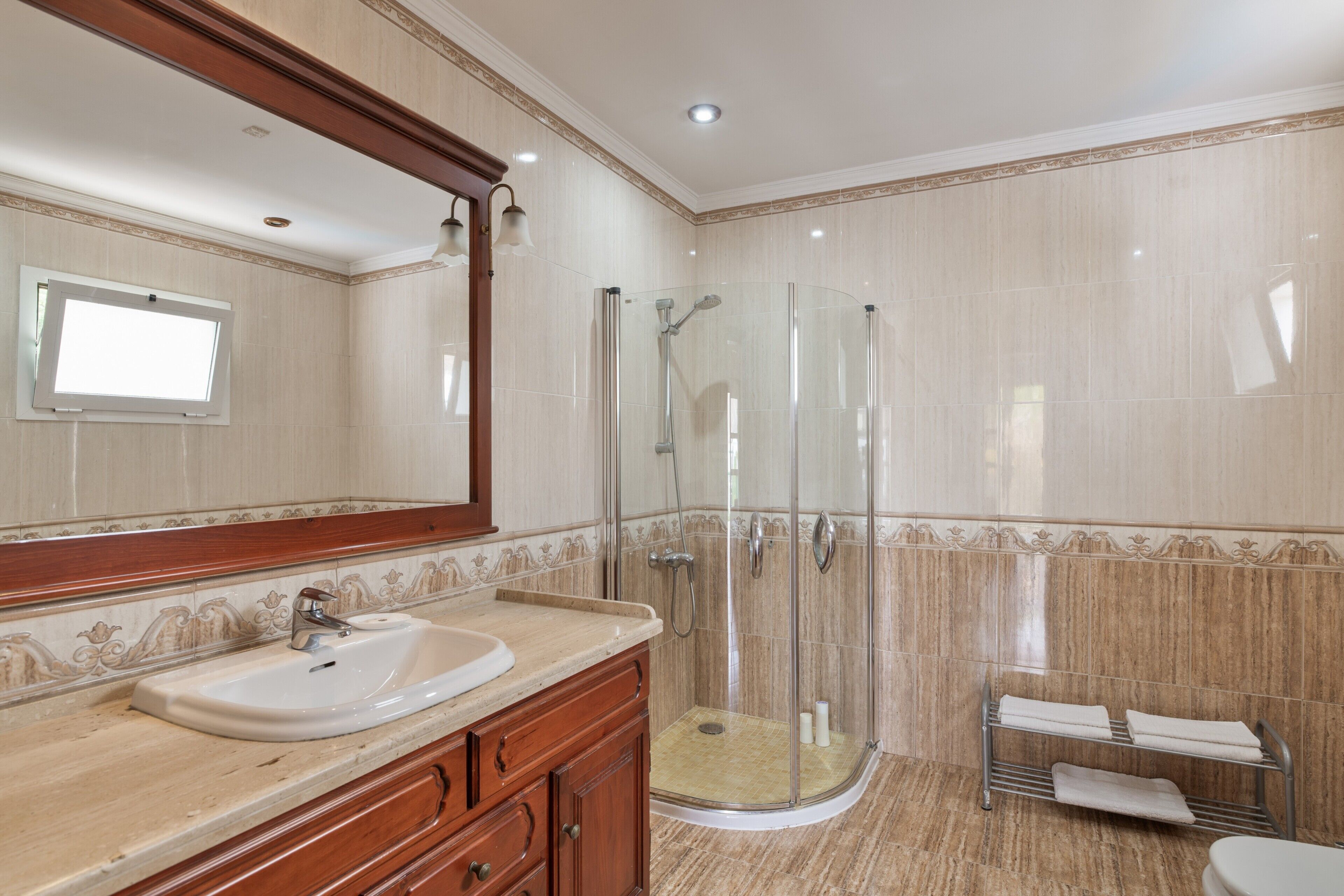 Un baño con lavamanos, espejo, ducha y toallero.