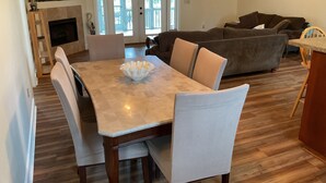 A dining area with a marble table and wicker chairs, a living room with a sofa and a painting, and a fireplace.