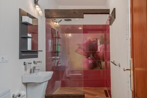 A bathroom with a white sink, a mirror, a towel rack, a shower, and a toilet.