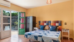 A bedroom with a bed, a green door, a wardrobe, a nightstand, and a hanging light fixture.