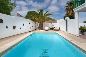 Una piscina con una palmera, una silla de descanso y una mesita.