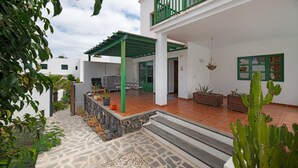 Una casa moderna con un patio, mobiliario exterior y plantas en macetas.