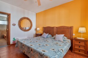 Un dormitorio con una cama, cabecera de madera, mesitas de noche, un espejo y una planta en maceta.