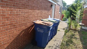 Una fila de contenedores azules para reciclaje junto a un muro de ladrillo.