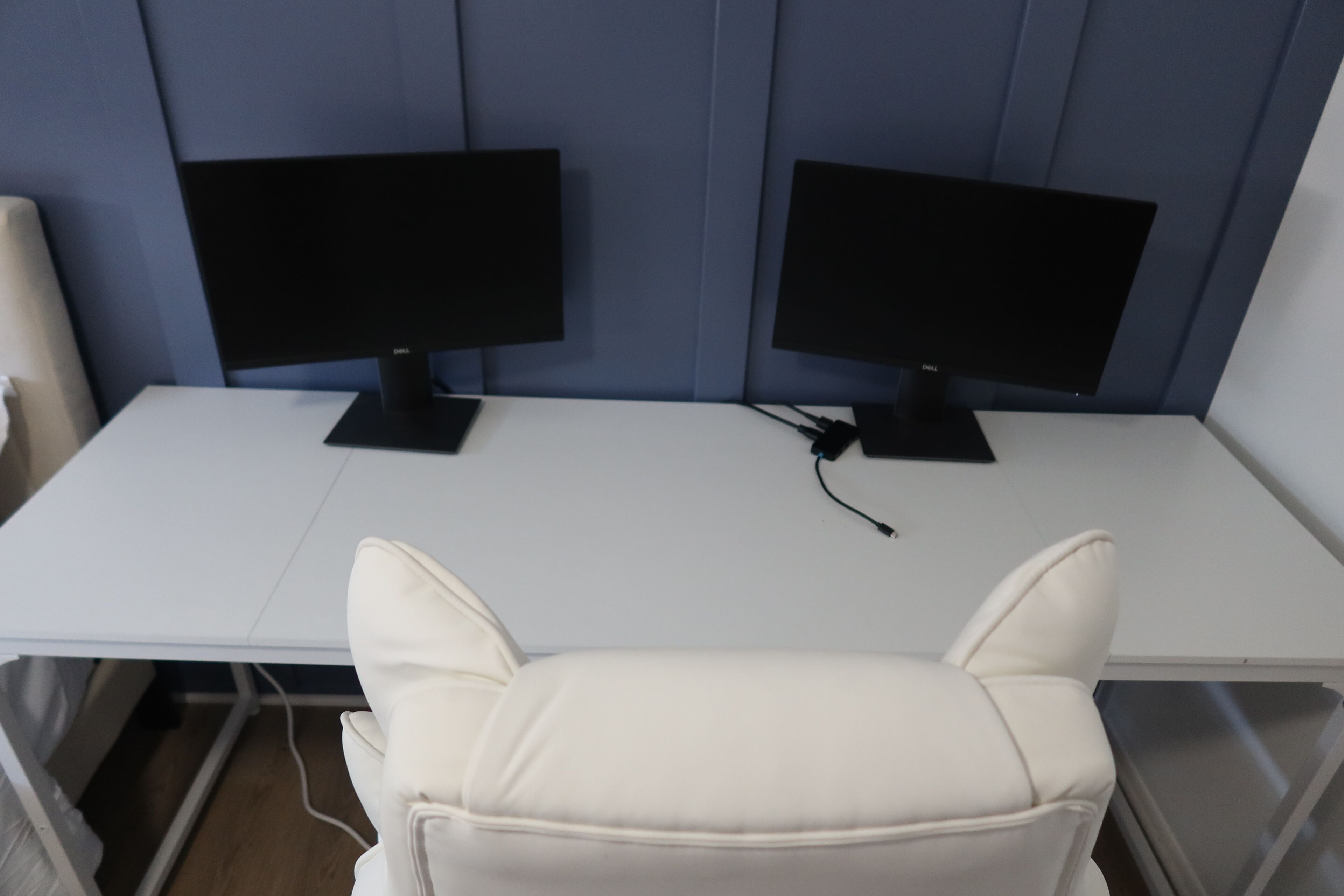 Een witte bureaustoel voor twee zwarte monitoren op een wit bureau.