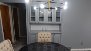 Un comedor con una mesa redonda negra, sillas tapizadas en tono beige y una araña.