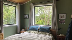 A bedroom with a bed, two bedside tables, a nightstand, a lamp, and a window with curtains.