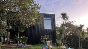 A modern house with a large window, a small deck, and a grassy yard with a tree and a playset.