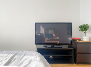 Ein Hotelzimmer mit einem Bett, einem Fernseher auf einem Schrank, einem kleinen Schreibtisch mit einer Pflanze und einigen Büchern.