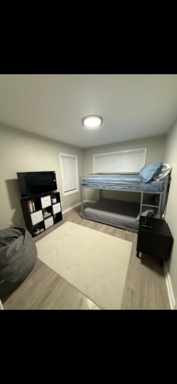 A room with a bunk bed, a black TV stand, a white desk, and a beige rug. - Uptown Modern Escape - 4bd/2ba (Memphis)