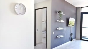Een modern interieur met een klok, een grijze wand met planken, een televisie en een deur die naar een andere kamer leidt.