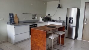 Een moderne keuken met een centraal eiland, roestvrijstalen apparatuur en een hanglamp.