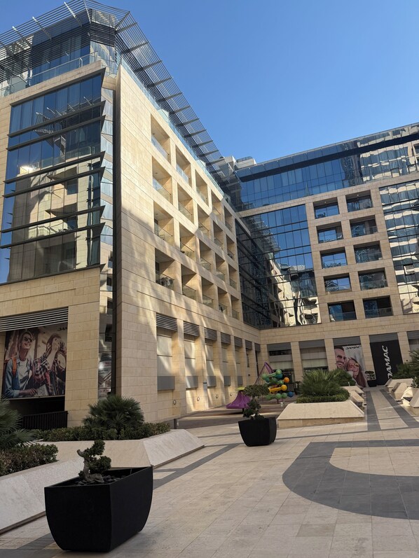A modern building with a glass facade and a courtyard with potted plants and seating areas.
