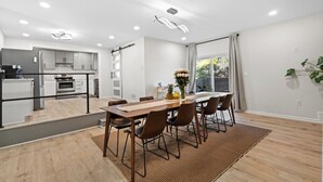A modern kitchen with stainless steel appliances, a dining area with a wooden table and chairs, and a large window with curtains.