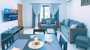 Ein modernes Wohnzimmer mit Essbereich, einer Sofagarnitur, einem Deckenventilator und einem an der Wand befestigten Flachbildfernseher.