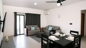 Ein modernes Wohnzimmer mit einer Couch, einem Esstisch für zwei Personen und einem Deckenventilator.