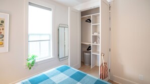 A bedroom with a bed, a window, a mirror, a closet, and a plant.