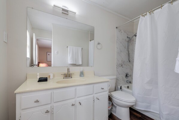 A bathroom with a white sink, mirror, and toilet, a shower with a white curtain, and marble-patterned walls. - Spacious 5-bedroom House in Gorgeous Olive Branch #811 (Olive Branch)