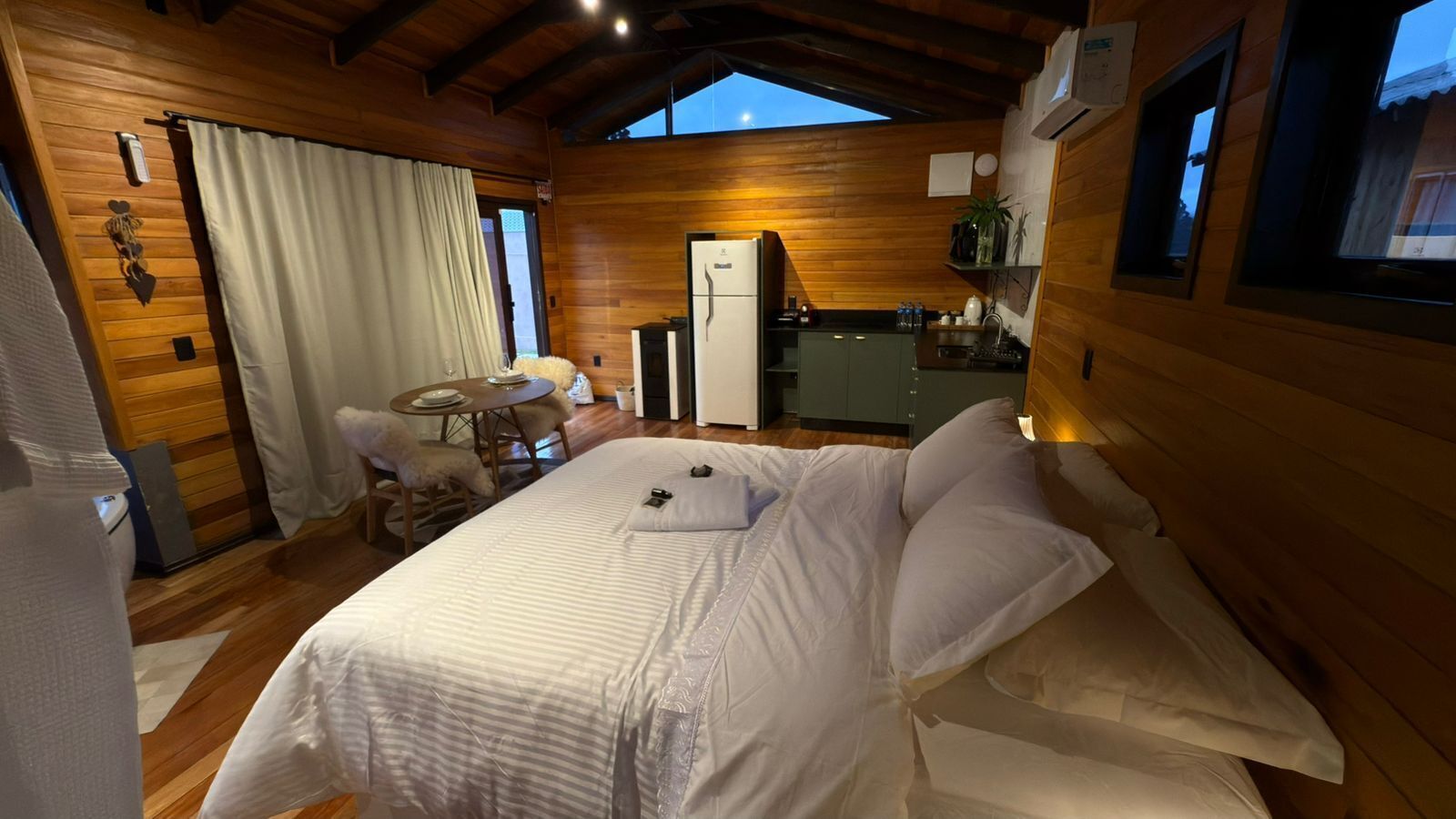 Une chambre confortable avec un grand lit, une petite table avec des chaises, un réfrigérateur et une fenêtre donnant sur l’extérieur.