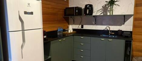 Cocina compacta con refrigerador blanco, gabinetes verde oscuro, techo de madera y salpicadero de mármol.