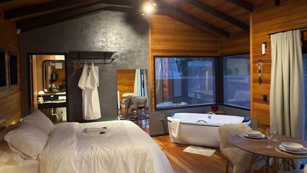 A cozy bedroom with a large bed, a small table, and a bathtub. - Chalé Cabernet - Vila Chamonix (Urubici)