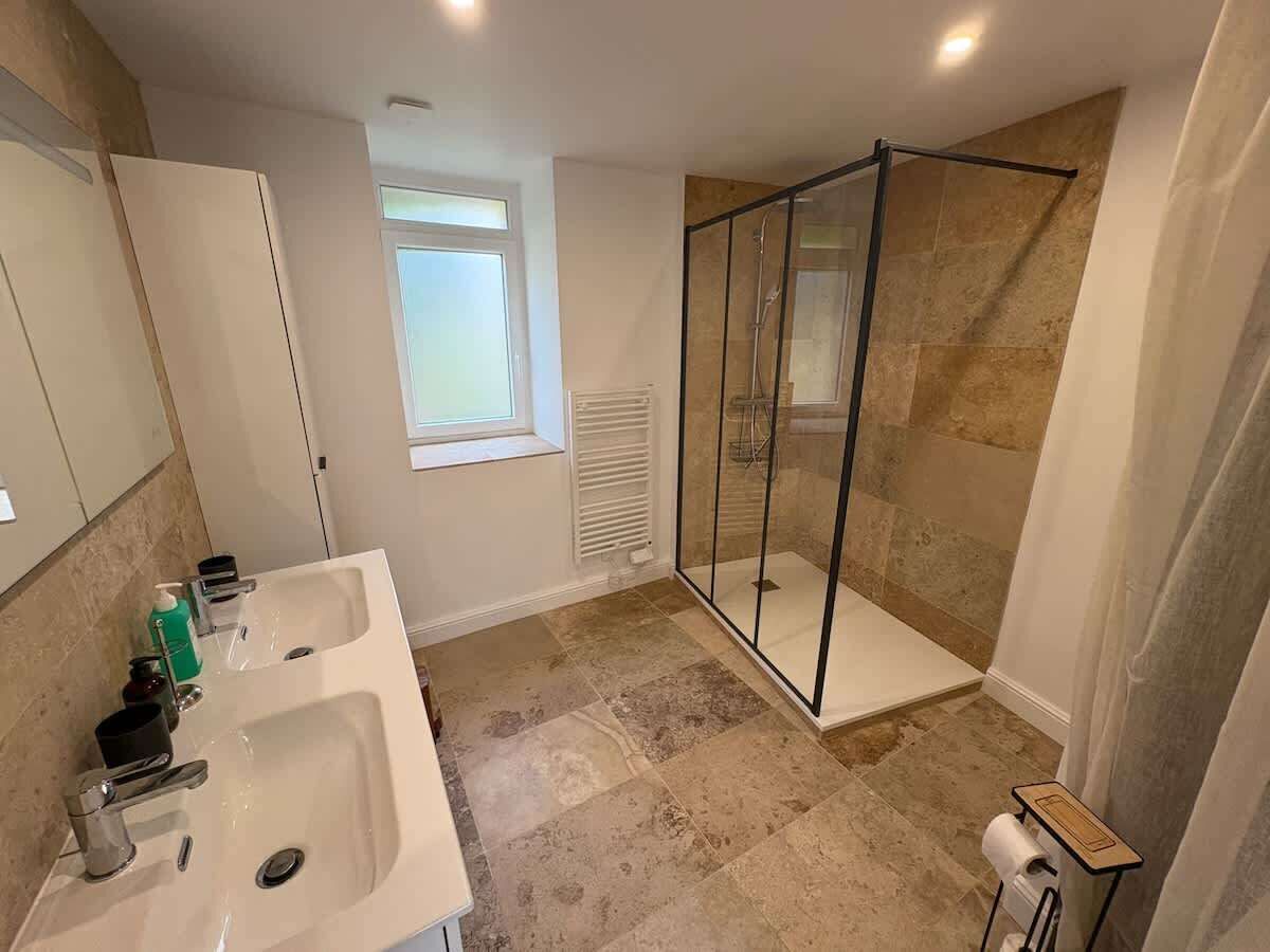 A bathroom with two sinks, a glass shower enclosure, and a window providing natural light.
