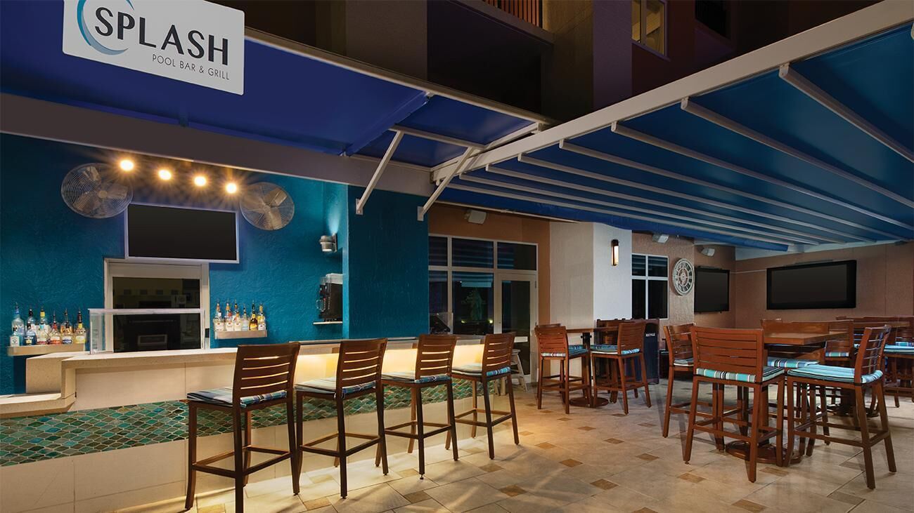 A pool bar with a blue and white color scheme, wooden chairs, and a bar counter with bottles.