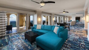 Un amplio vestíbulo de hotel con un sofá grande color turquesa, una zona de comedor y vistas al océano a través de un arco abierto.