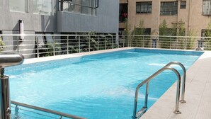 Ein Außenpool mit Metallgeländern, umgeben von einer gefliesten Terrasse und angrenzenden modernen Gebäuden mit Balkonen.