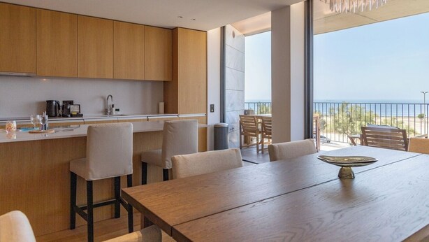 Una cocina moderna con armarios de madera, un comedor con mesa y sillas de madera, y vistas al mar a través de amplios ventanales.