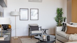 Una sala de estar moderna con un sofá, dos mesas redondas, una silla y una lámpara de pie.