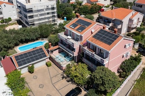 A multi-story building with a rooftop pool and solar panels, surrounded by trees and other residential buildings.