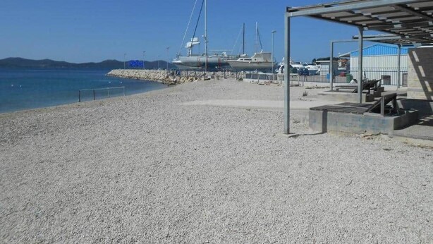 A pebbled beach with boats docked in the background.