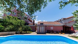 A swimming pool with a red-roofed building in the background, surrounded by greenery.