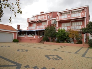 A multi-story building with balconies, a covered entrance, and a paved courtyard.