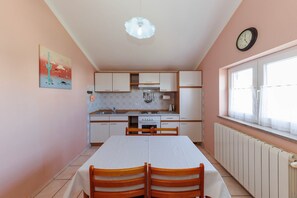 Una cocina compacta con una mesa, sillas, un reloj y una ventana con cortinas.
