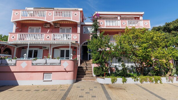 Un bâtiment rose à deux étages, doté de balcons, d’un escalier et de plantes en pot.