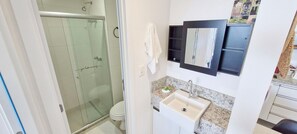 Un baño con cabina de ducha de vidrio, inodoro, lavamanos con espejo y una toalla colgada en la pared.