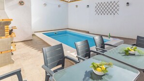 Un área junto a la piscina con una pileta rectangular, sillas negras y una mesa con un cuenco de limones y hierbas.
