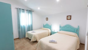 Una habitación con dos camas, una ventana con cortinas, una mesita de noche y una lámpara de pared.